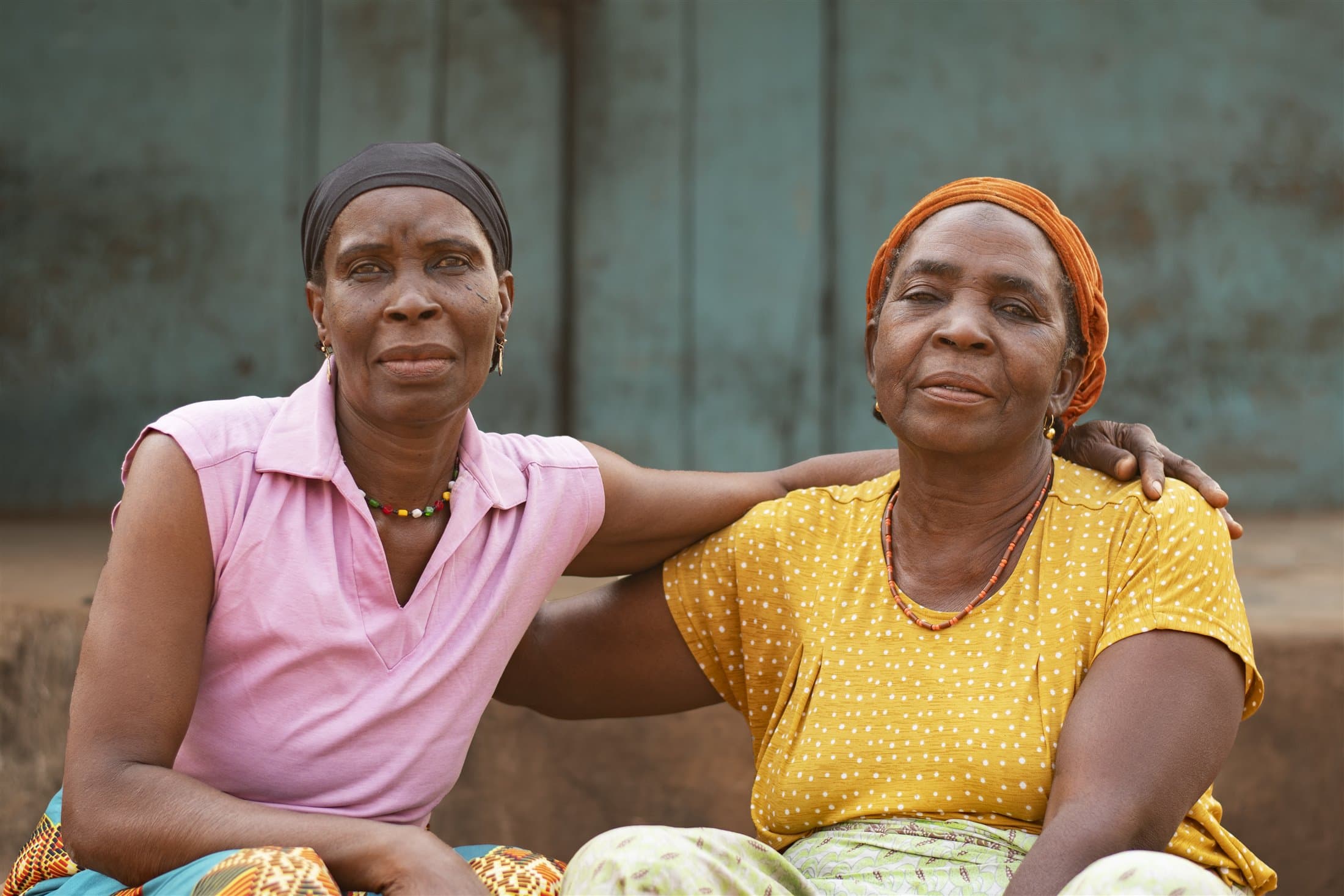 Two older African women sitting closely together with an arm around one another